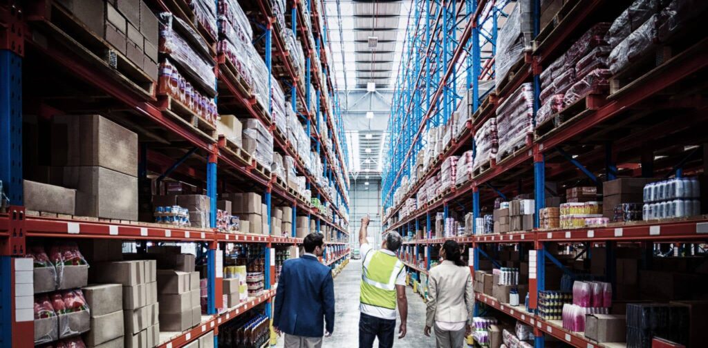 A group of people walking through an aisle in a warehouse.