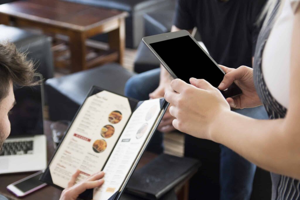 Two people are holding a tablet and looking at the menu.