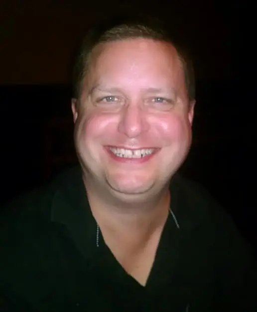 A man smiling for the camera in front of a dark background.