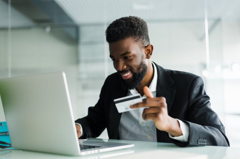 A man holding a credit card in front of his laptop.